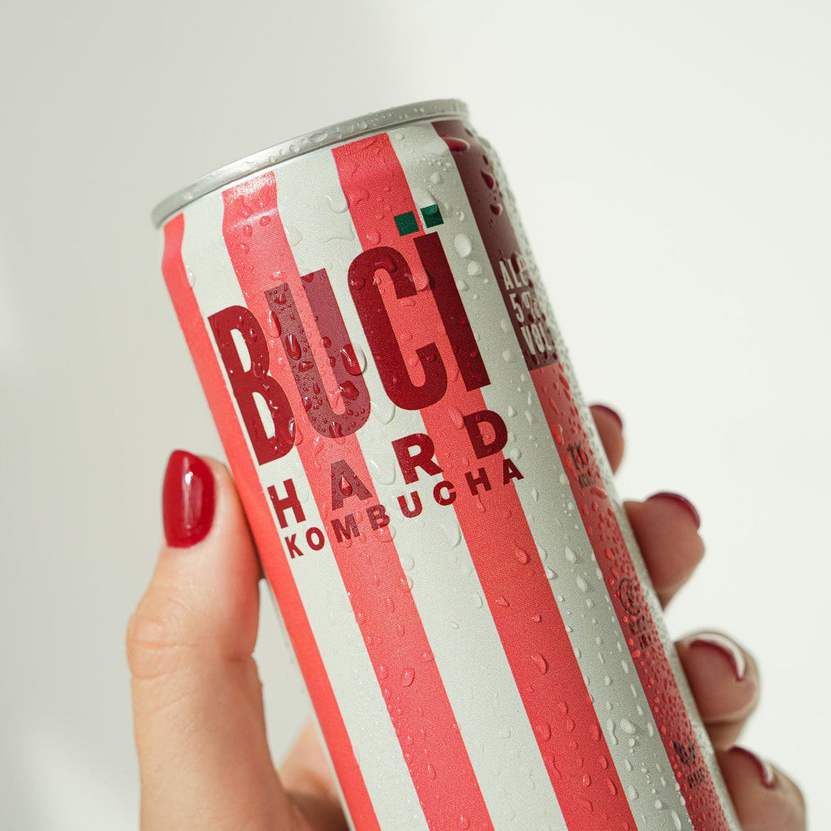 Hand holding a can of Buci Hard Kombucha with red and white striped design.
