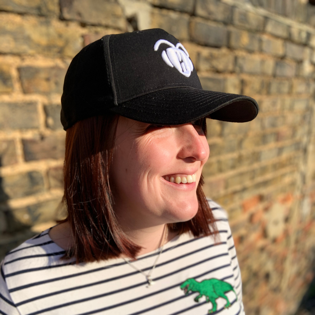 Woman wearing black Phoebee cap with bee logo smiling against a brick wall