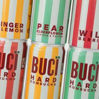 Multiple cans of BUCÏ Hard Kombucha flavours stacked on each other.