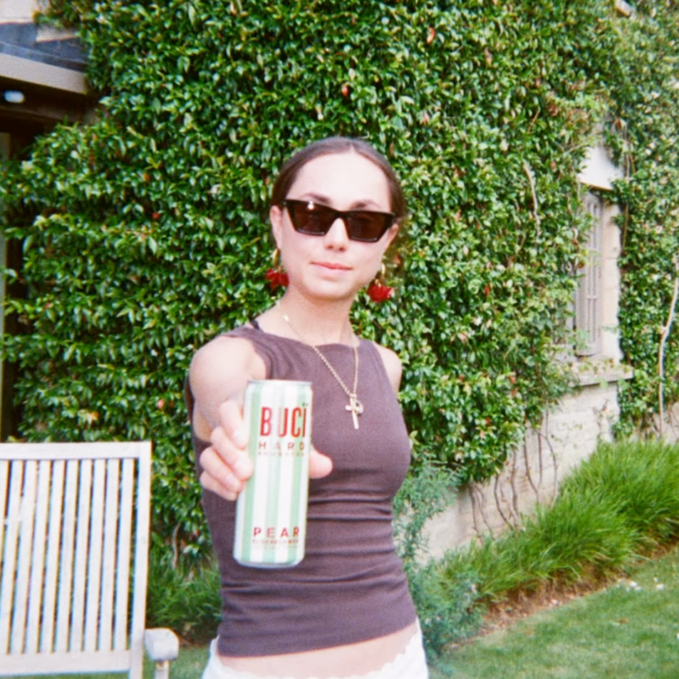 A woman holding a can of BUCI Pear & Elderflower Hard Kombucha in a grassy setting.
