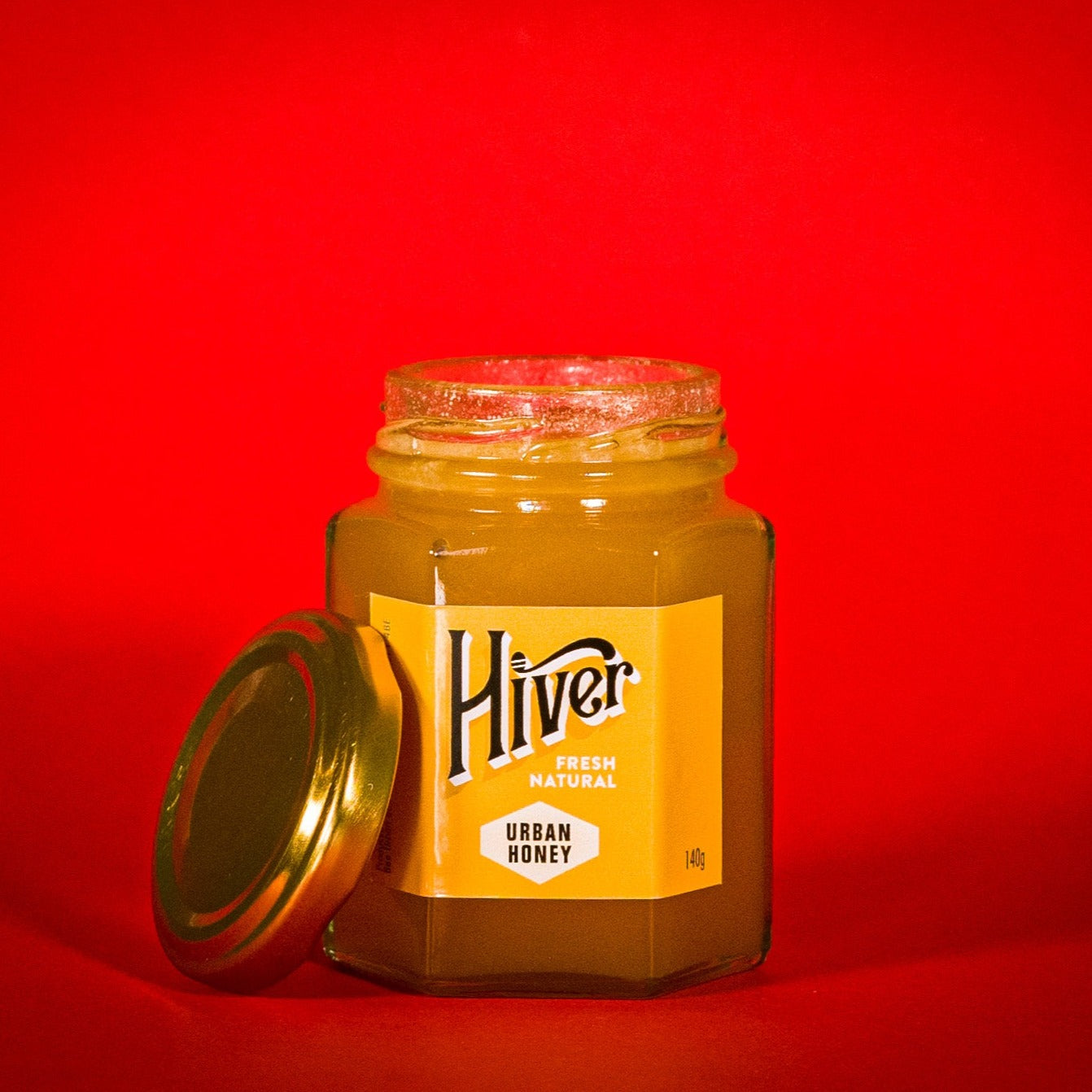 Open jar of Hiver London Urban Honey with lid removed against a red background