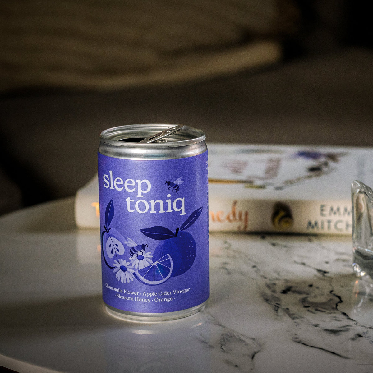 A Sleep Toniq can beside a lit candle on a marble table in a dim room