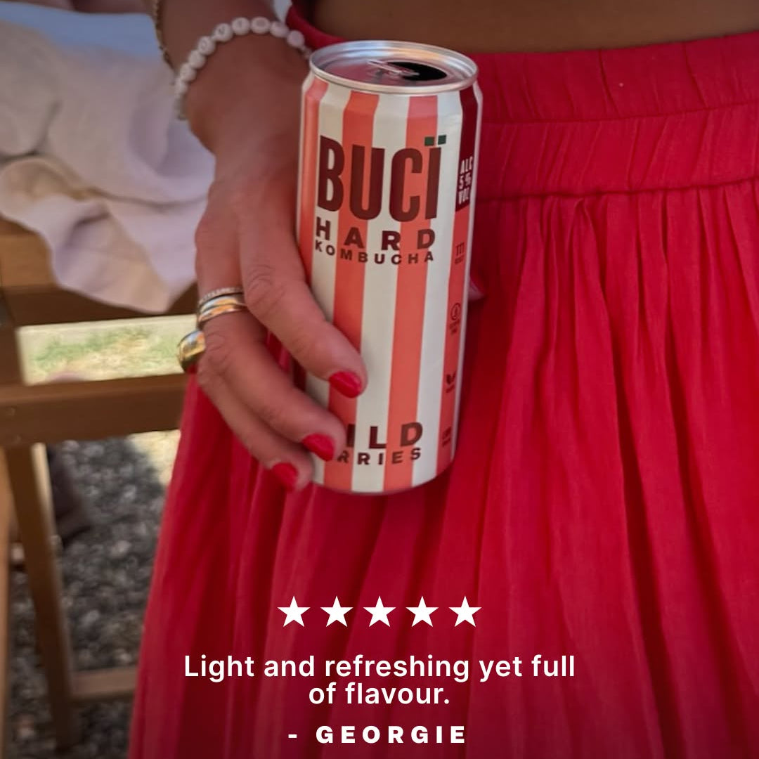 Person in a red dress holding a striped can hard kombucha Buci alcoholic