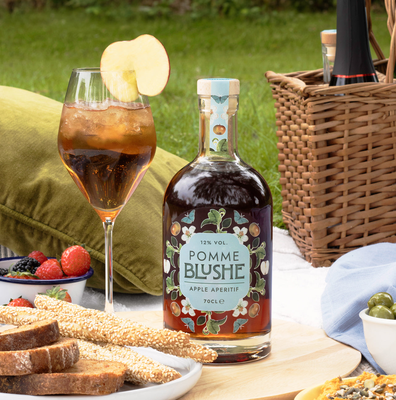 A bottle of Pomme Blushe apple aperitif and cocktail in a picnic setting.